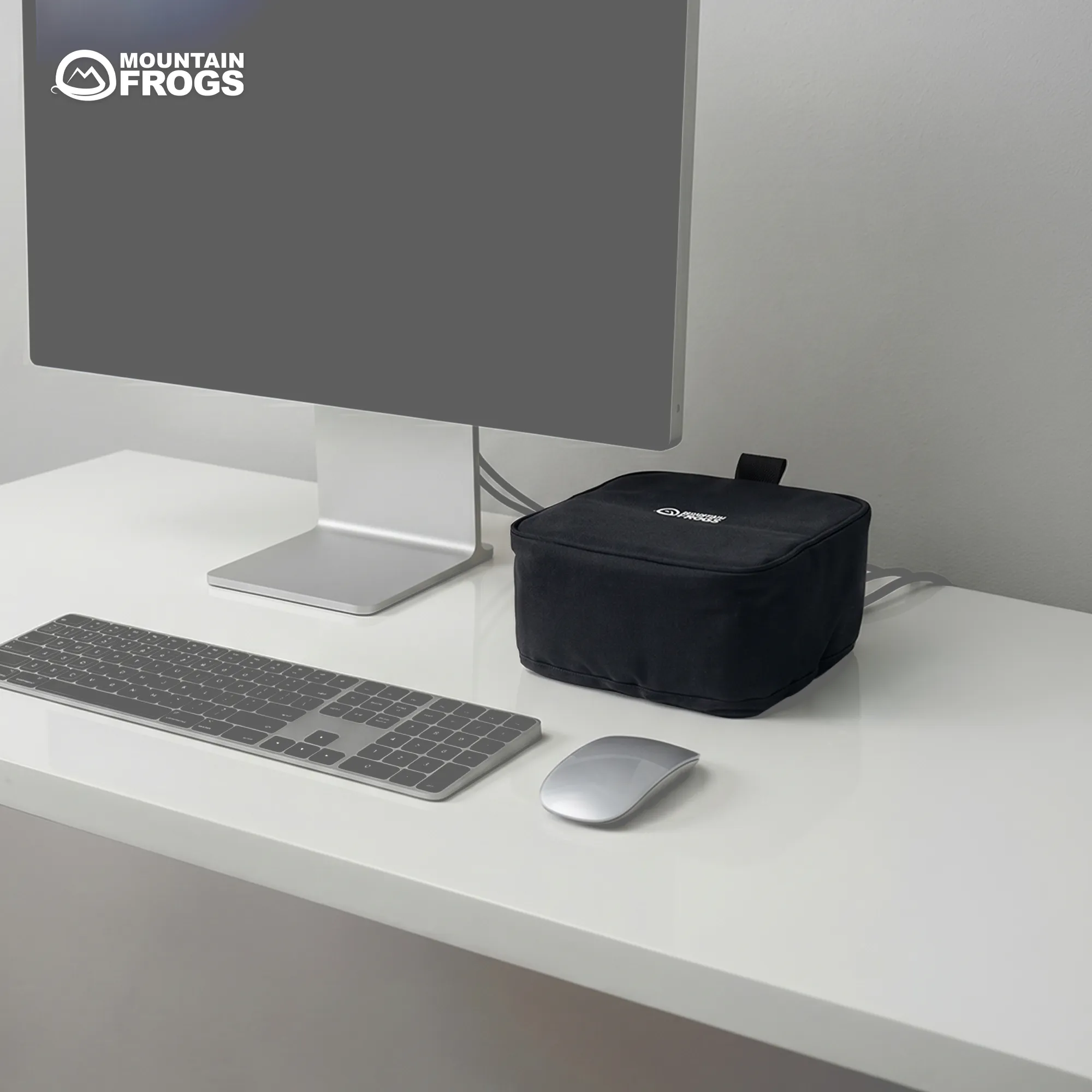 Minimalist modern home office desk setup with a silver desktop monitor, magic keyboard, mouse, and a covered Mac Studio in a black fabric sleeve.