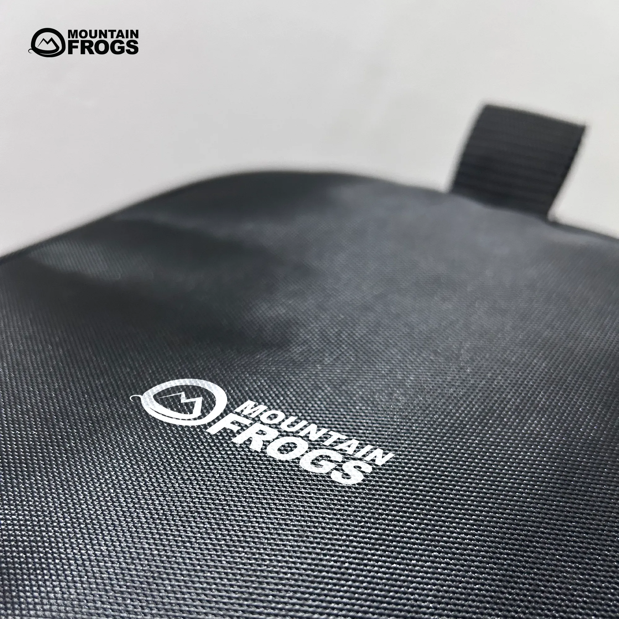 Macro close-up shot of the premium water-resistant polyester fabric texture featuring the crisp white Mountain Frogs brand logo print.
